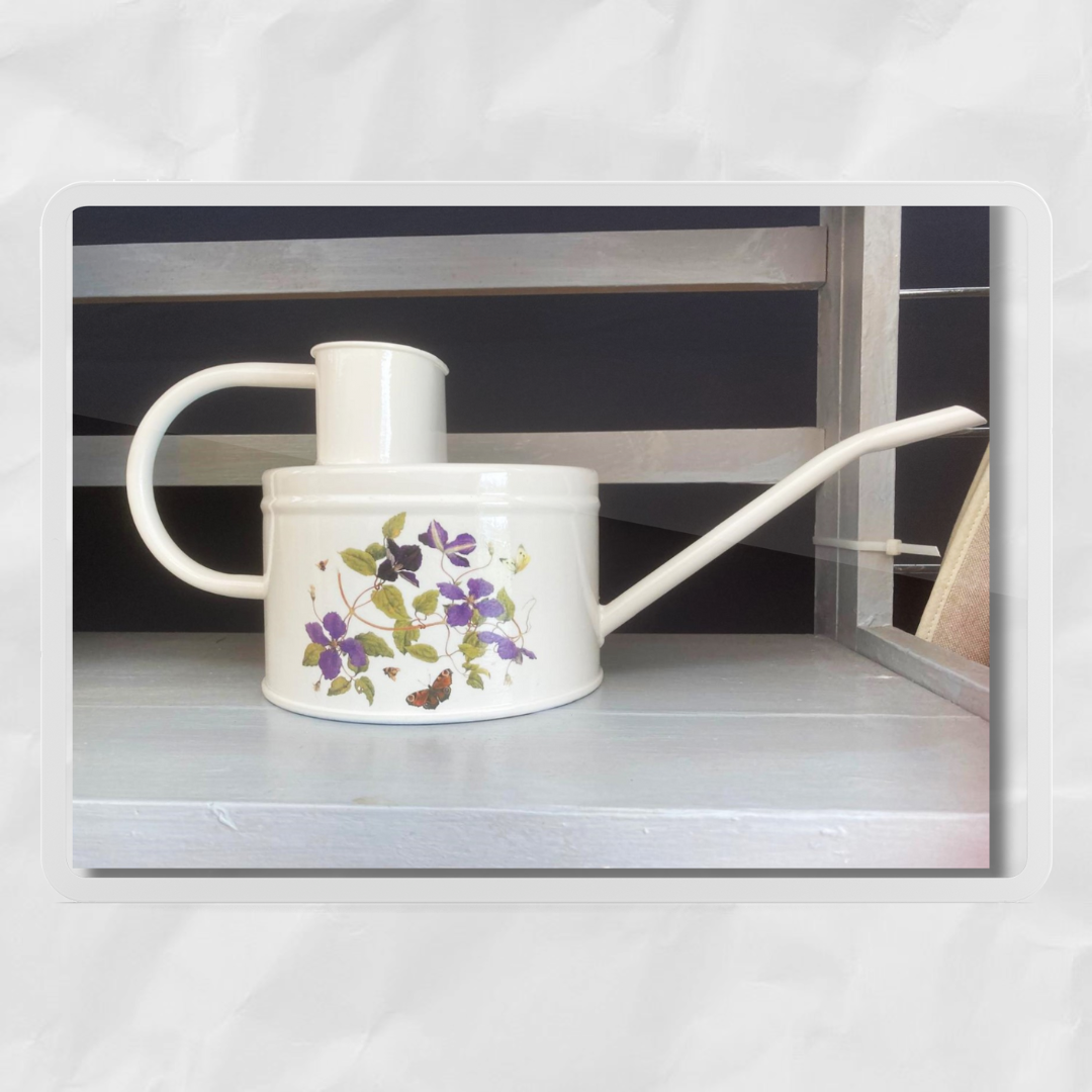 A white, off-white, and multicolored floral patterned watering can made from galvanized steel, featuring a long spout and handle.