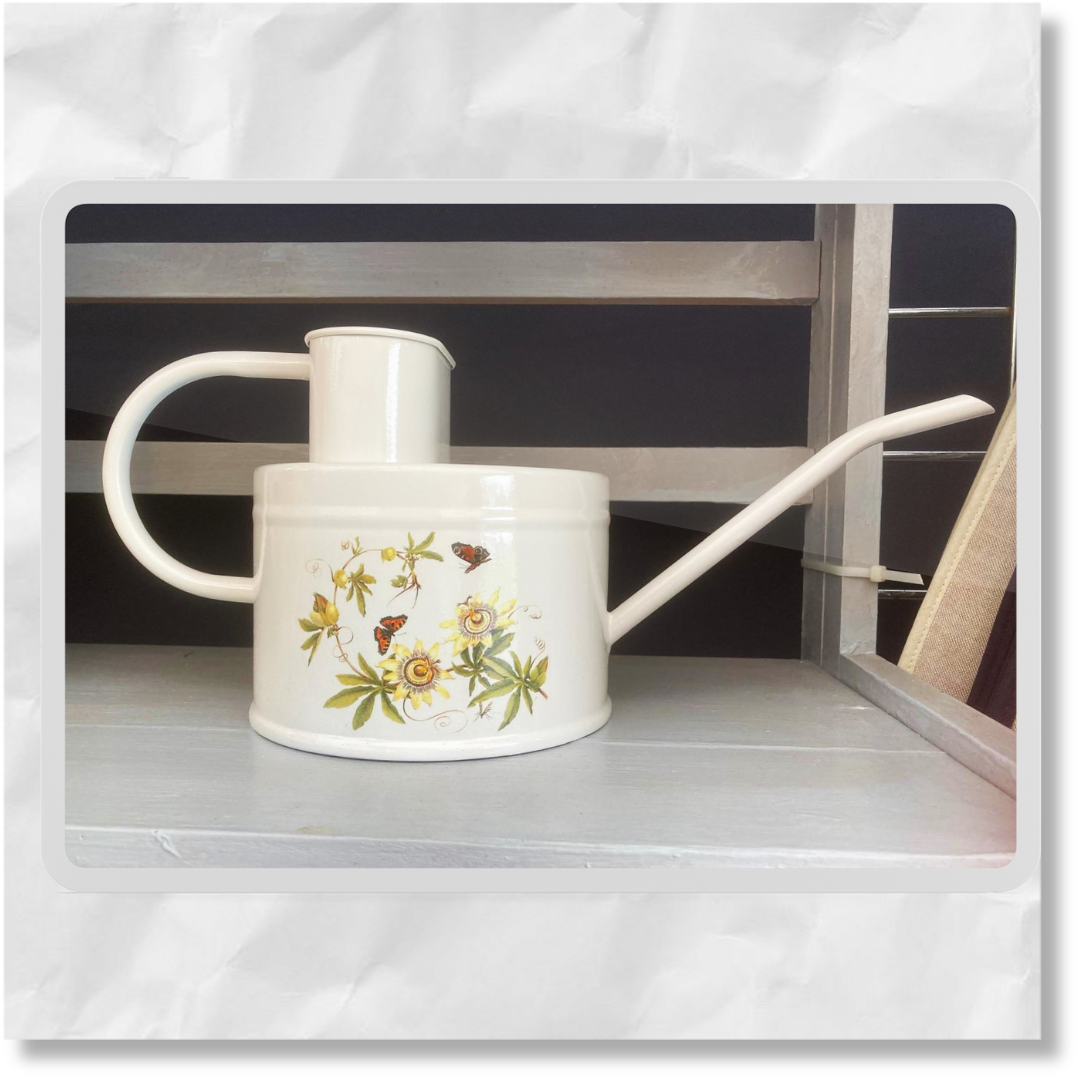 A white, passion flower design watering can made from galvanized steel with a hand-painted floral pattern.