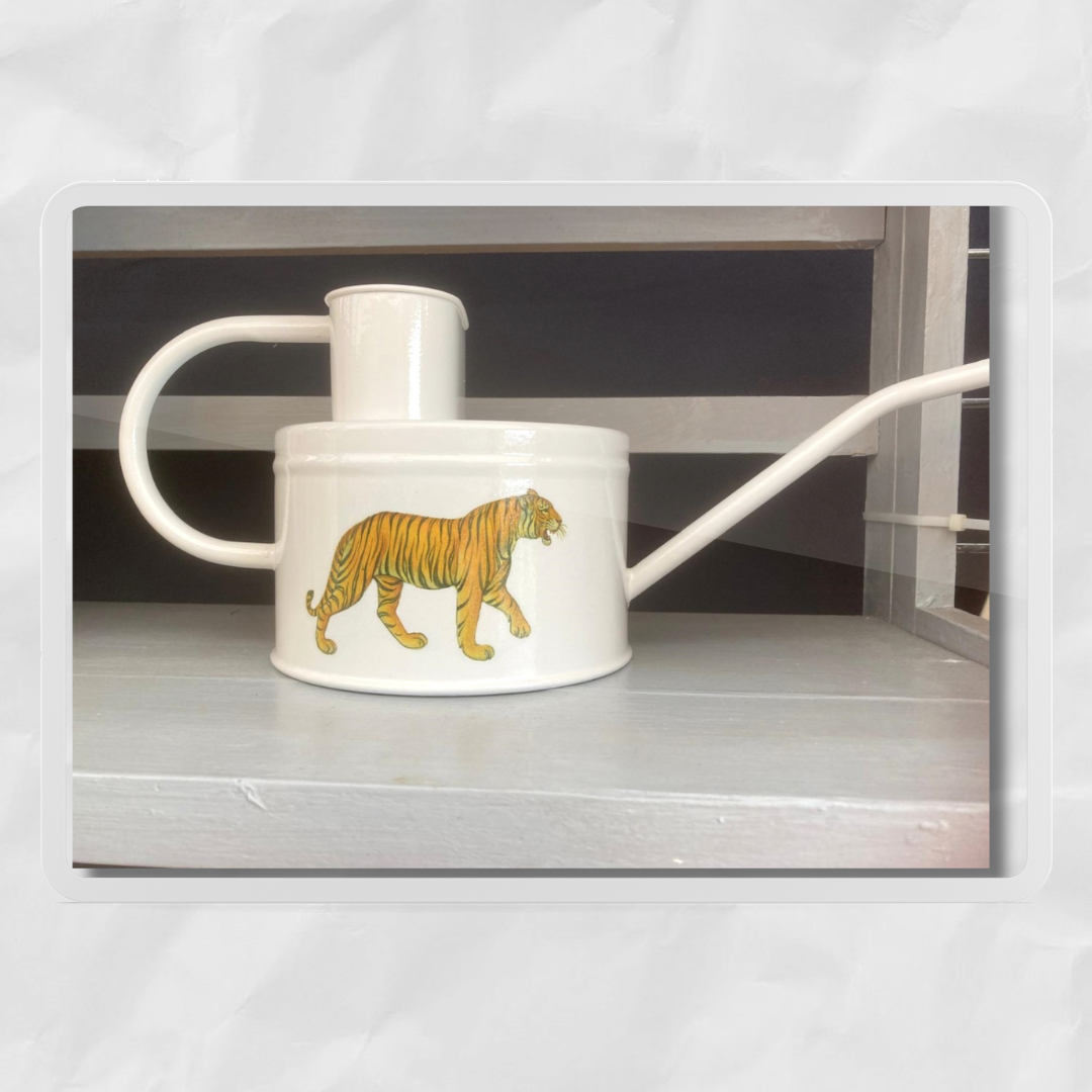A white watering can with a hand-painted tiger design on the side, standing upright against a dark background.