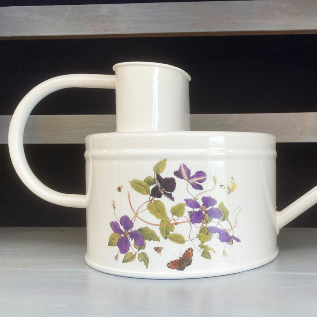 A white, off-white, and multicolored floral patterned watering can made from galvanized steel, featuring a long spout and handle.