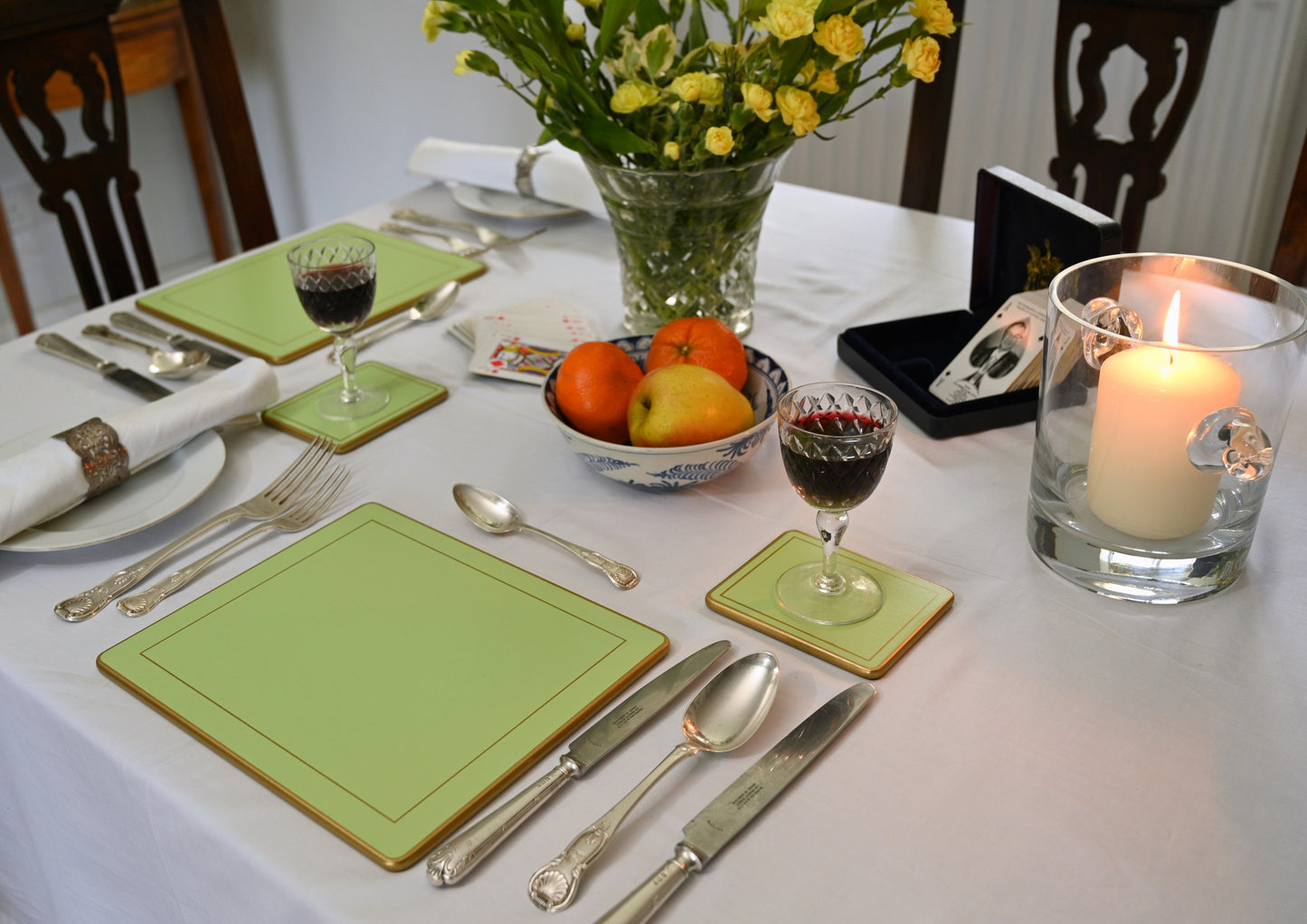 Dining table setting with green placemats, silverware, and a bowl of fruit.