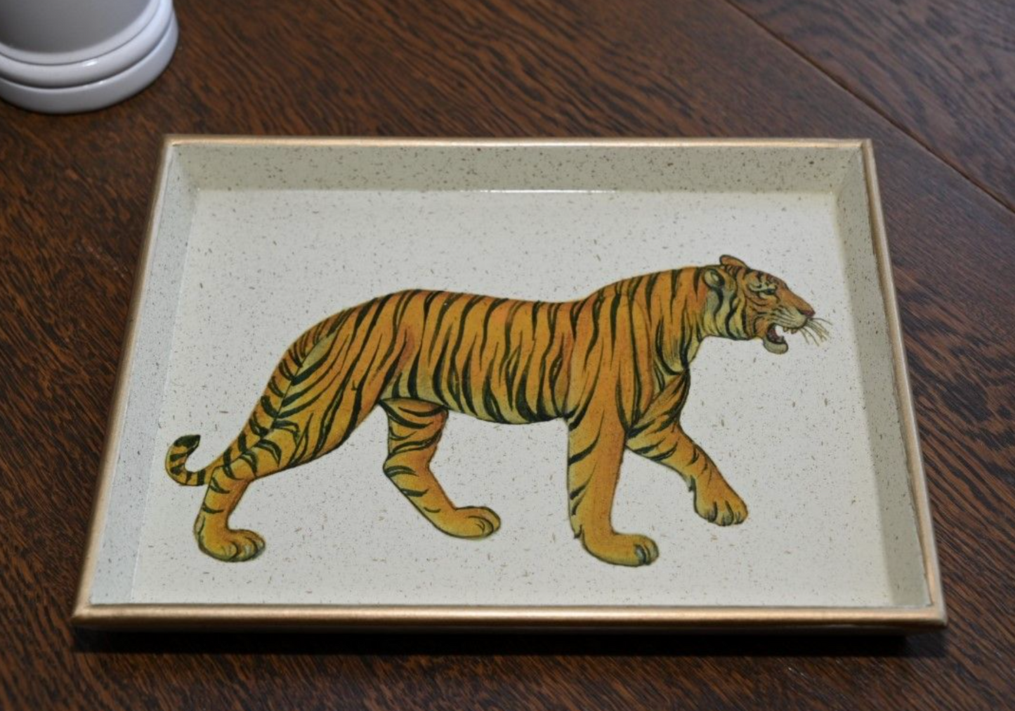 A decorative tray featuring a gilded gold rim and a baize base, with a printed tiger design on a wooden table background