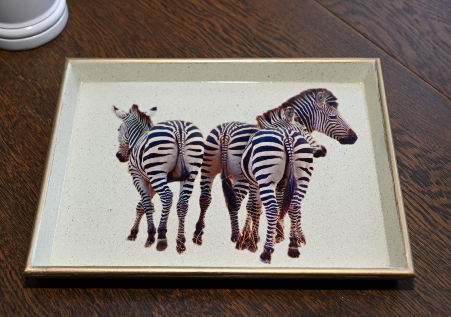 A wooden lacquered tray with a gilded gold rim and baize base, featuring an image of zebras in the centre on a wooden table background